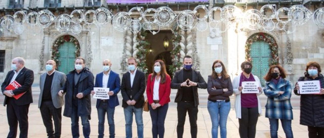 La oposición protesta frente al Ayuntamiento de Alicante por la nueva ordenanza contra la mendicidad y la prostitución mientras el bipartito cuelga en el balcón una pancarta contra la violencia machista. /