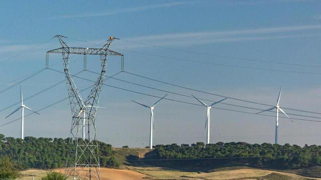 Una torre de la xarxa de transport d’electricitat i un parc eòlic.