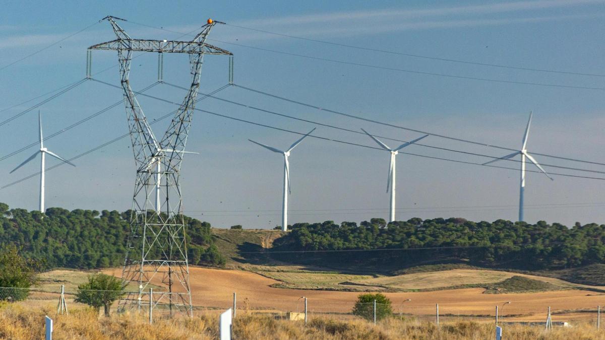 Una torre de la red de transporte de electricidad y un parque eólico.
