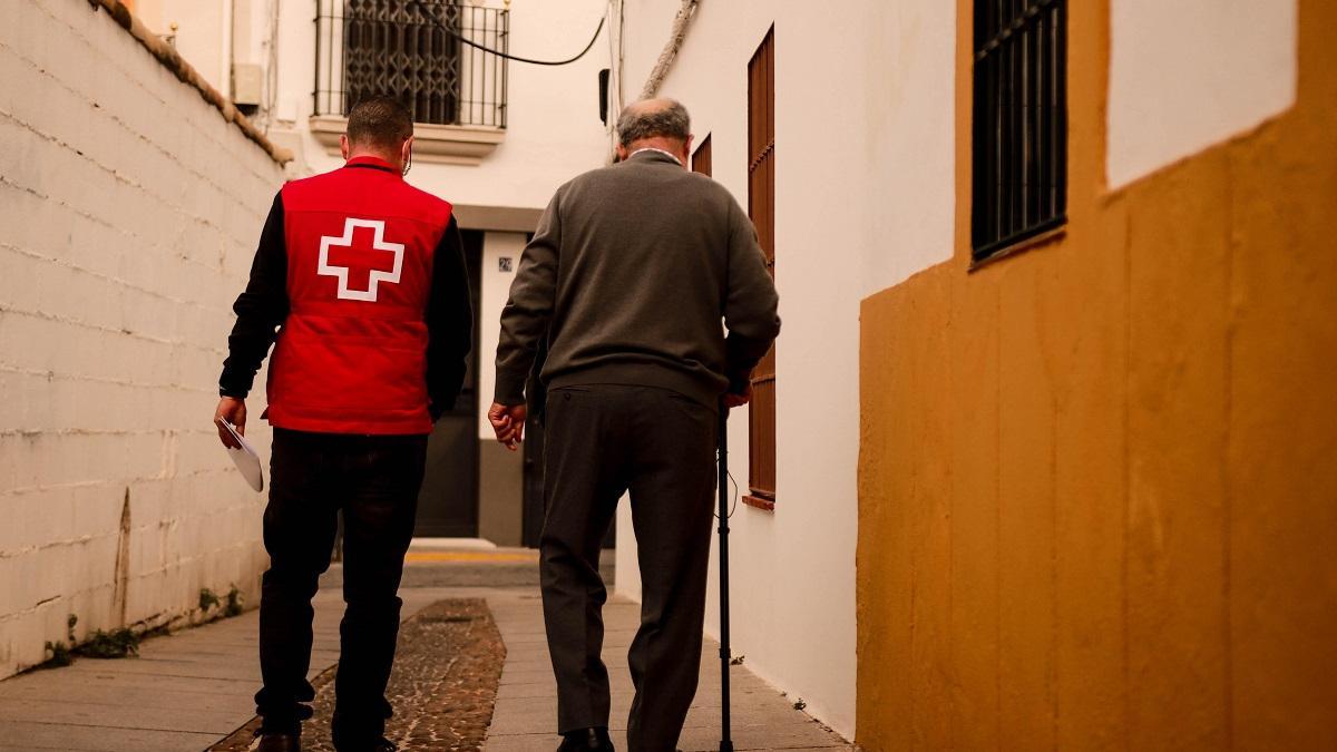 Un voluntario de Cruz Roja acompaña a una persona mayor.