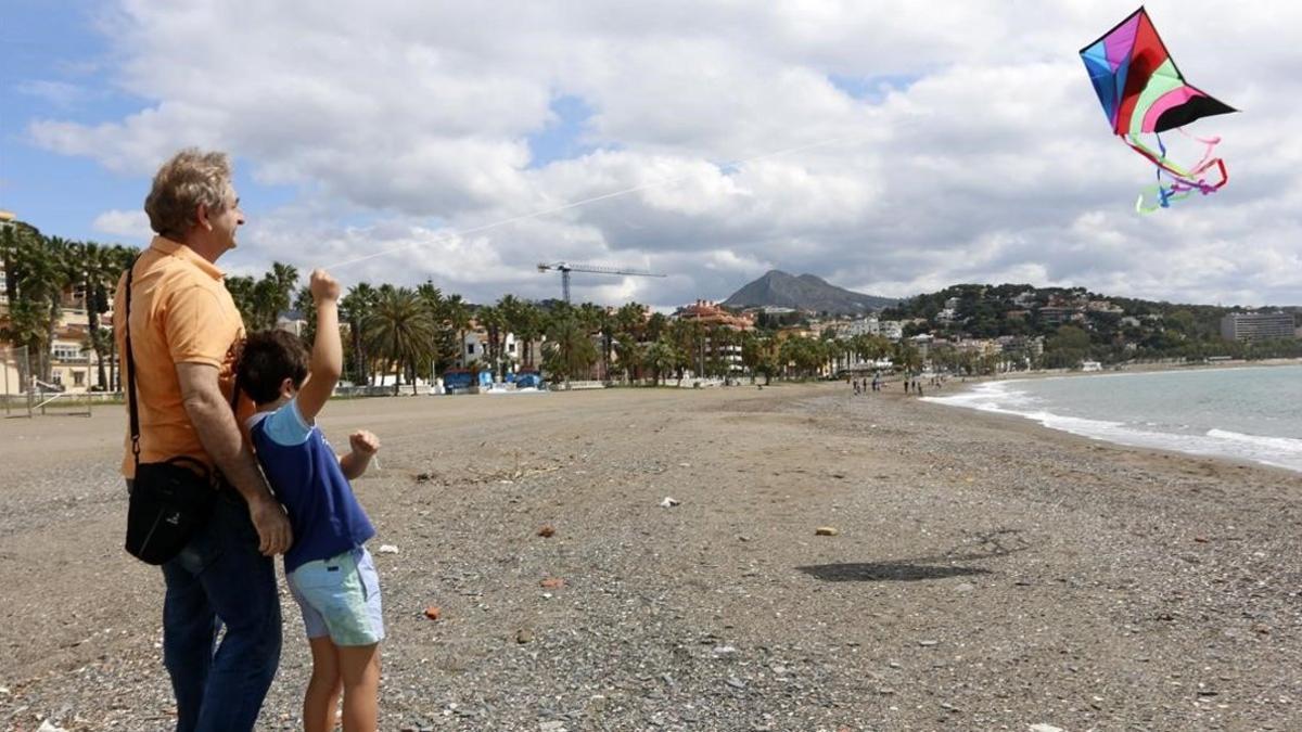 Un niño vuela una cometa junto a su padre en la playa de La Malagueta, este domingo, primer día en el que los menores de 14 años pueden salir durante el estado de alarma