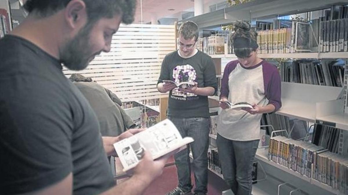 Joan, en primer plano, Joel y Alba consultan unos cómics en la biblioteca Ignasi Iglésias-Can Fabra.