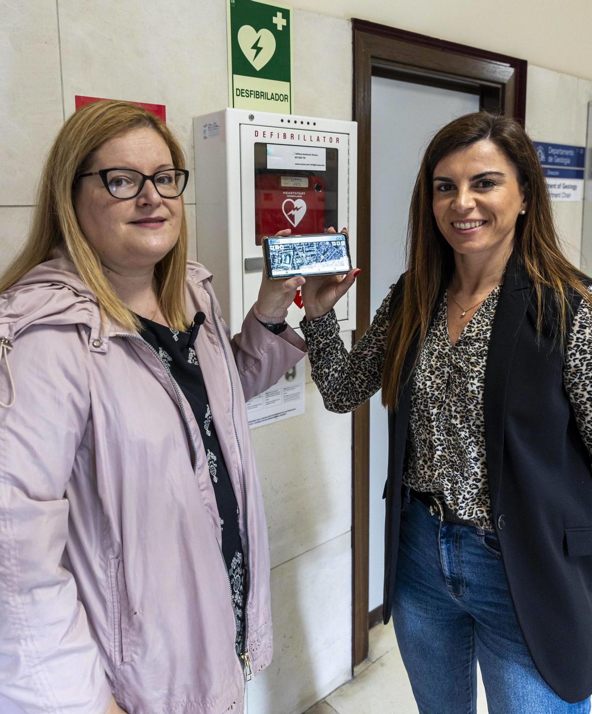 Tailí Pérez Rodríguez, de la Consejería de Ordenación del Territorio (a la izquierda), y Mari Luz Ardisana Sustacha, de la Consejería de Salud, muestran el desfibrilador instalado en la Facultad de Geología (Oviedo) y explican detalles de su funcionamiento. |  | DAVID CABO