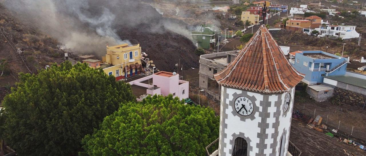 Foto del dron al sobrevolar el campanario de la iglesia del barrio con la lava engullendo varias viviendas de Todoque.