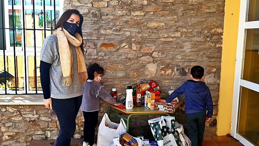 Una profesora posa con dos alumnos y los alimentos recogidos.