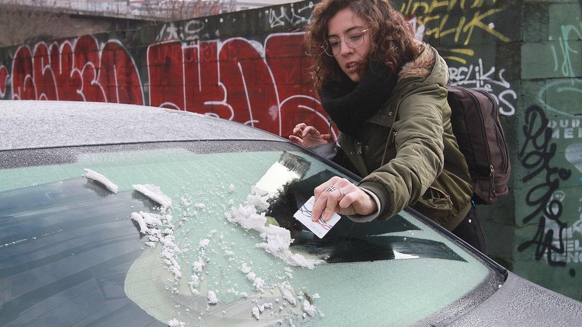 Una joven retira el hielo del parabrisas de su coche, en Ourense