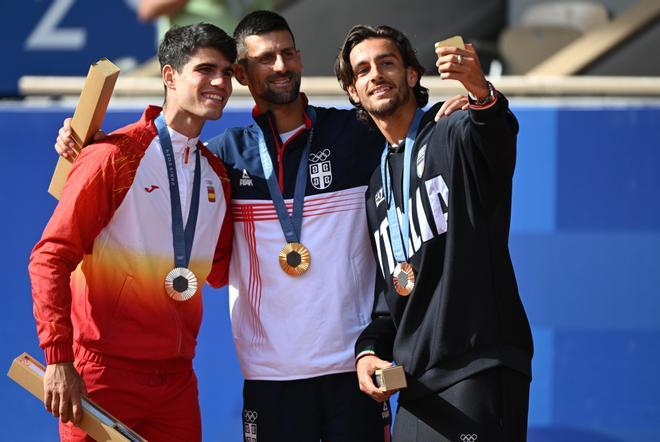 Carlos Alcaraz haciéndose un selfie con la medalla de plata en el podio junto a  Novak Djokovic, medalla de oro, y Lorenzo Musetti, medalla de bronce, tras la final individual masculina de tenis de los Juegos Olímpicos de París 2024.

