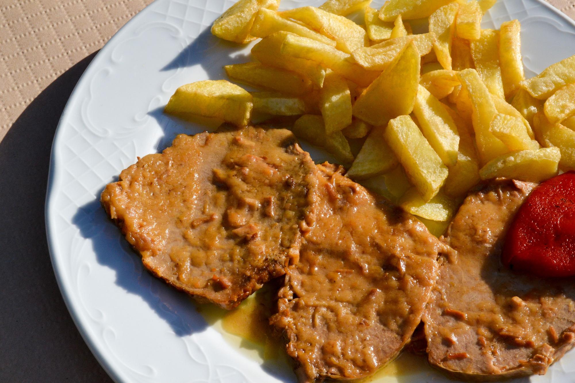 Ternera guisada acompañada de patatas fritas caseras y pimientos.