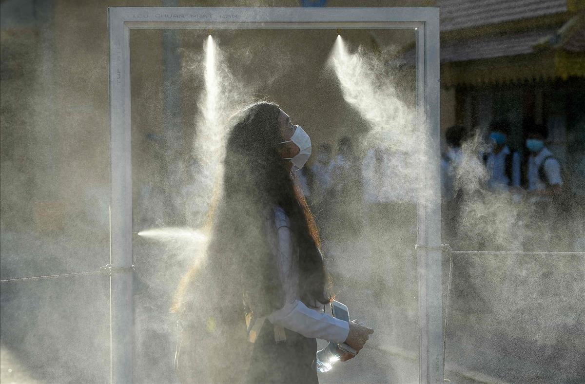 Una estudiante atraviesa una puerta equipada con spray desinfectante como parte de las medidas contra el coronavirus, en Phnom Penh.