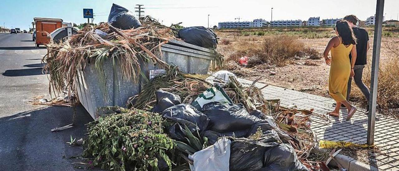 Una pareja pasa junto a un contenedor desbordado por la basura en la Vega Baja.