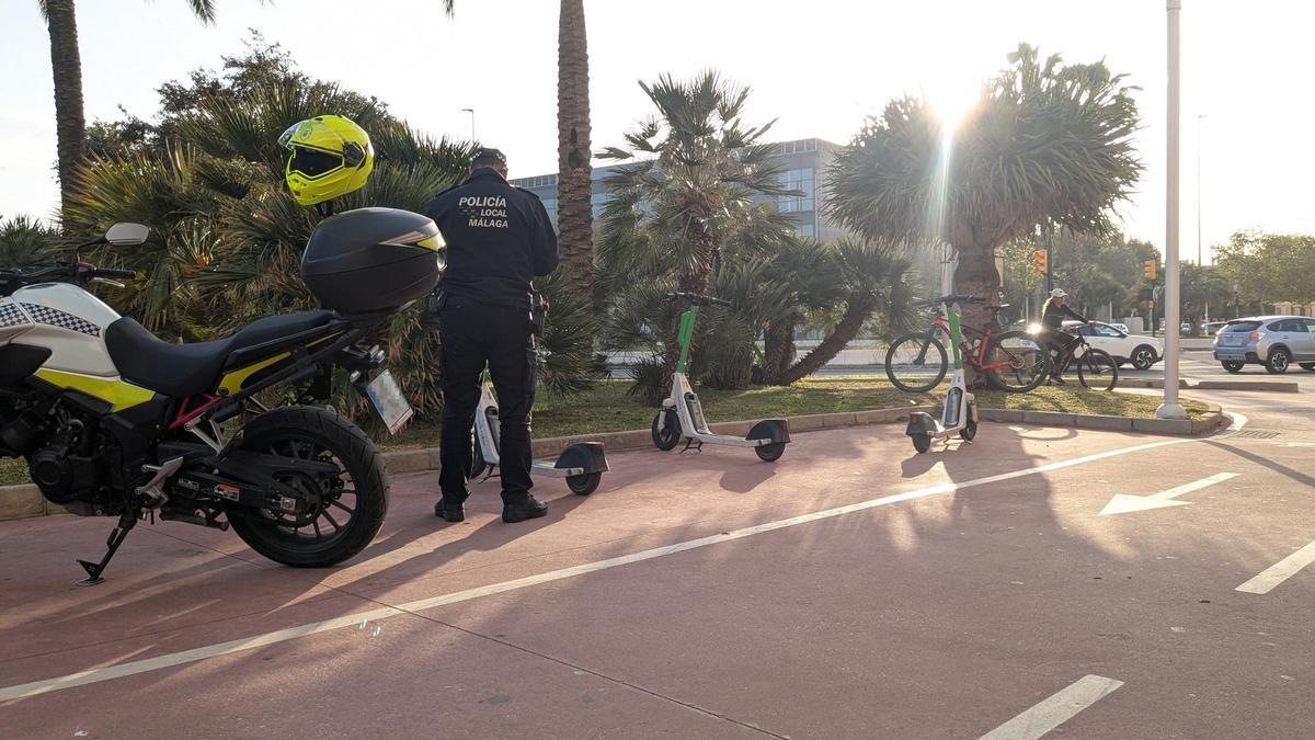 Un agente de la Policía Local sanciona a unos patinetes mal estacionados en el paseo marítimo Antonio Machado, en la playa de la Misericordia