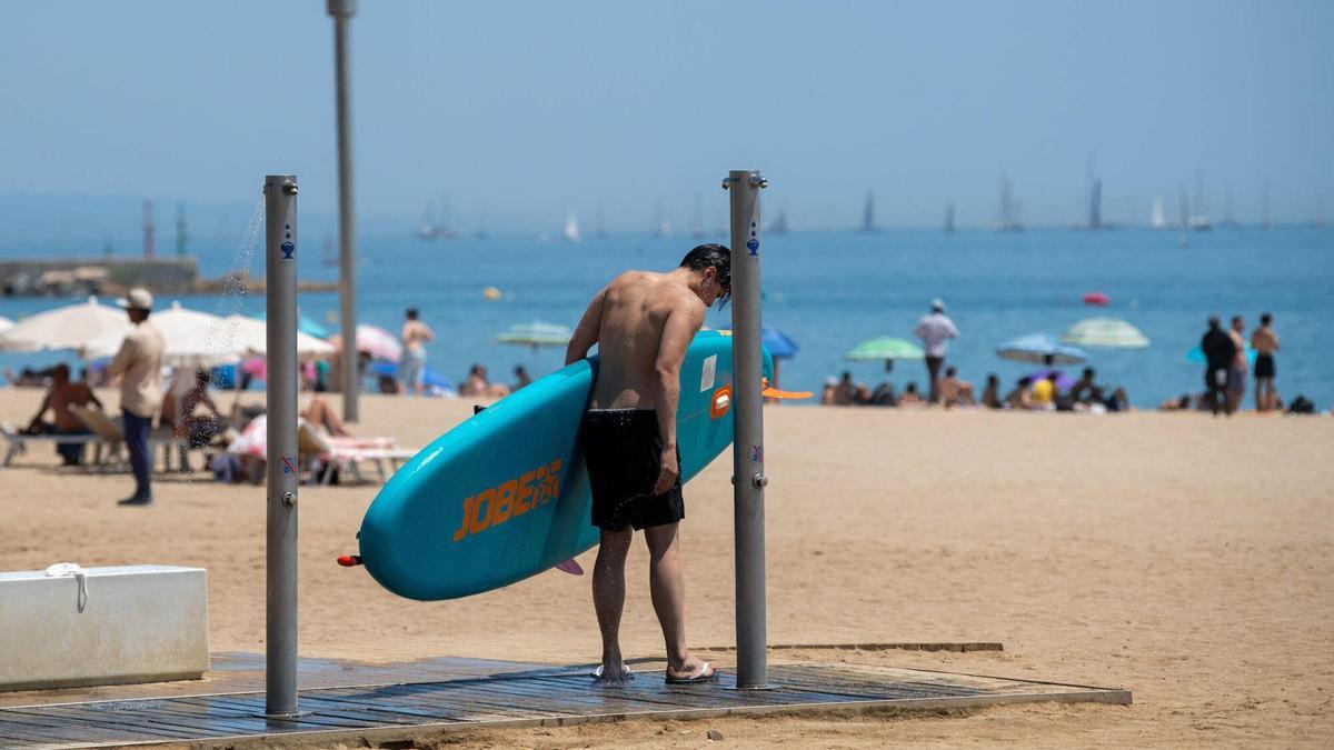 Un chico con una tabla de surf en las duchas de la playa de la Barceloneta.