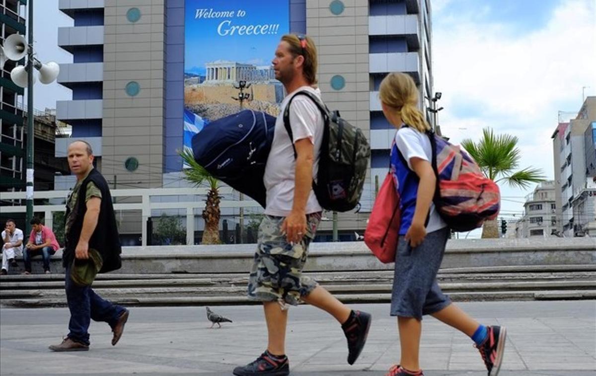 Turistas en la plaza de Omonoia frente a un cartel gigante que reza ’Bienvenidos a Grecia’.