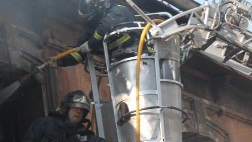 Dos bomberos trabajan en la tercera planta del inmueble, con el vehículo de altura.