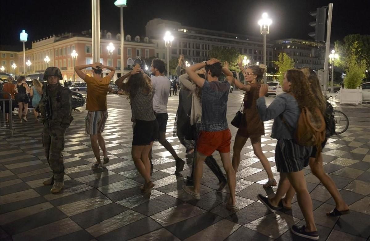 La gente cruza la calle con las manos en la cabeza en Niza, ante un control de soldados. 