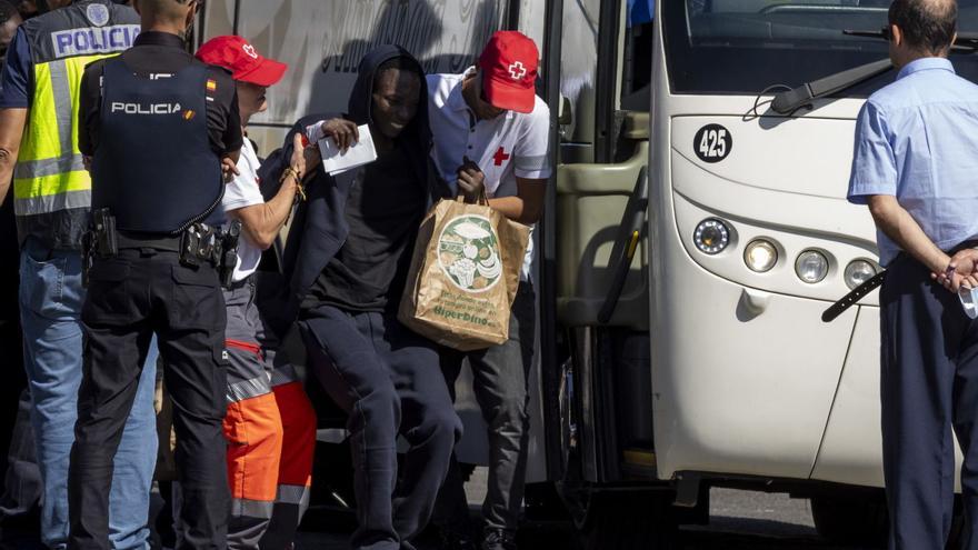 Un migrante es ayudado a subir a la guagua por el personal de la Cruz Roja tras ser atendido en el muelle de Arguineguín.