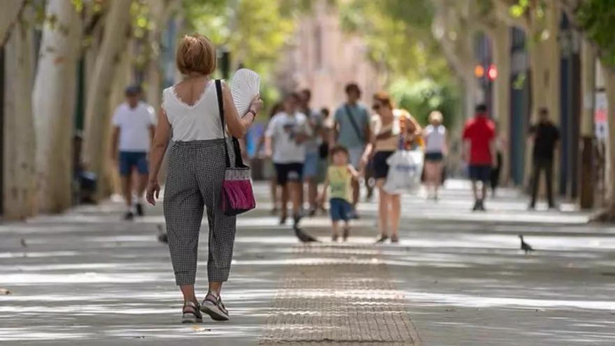 Una mujer se abanica a su paso por Alfonso X, en Murcia.