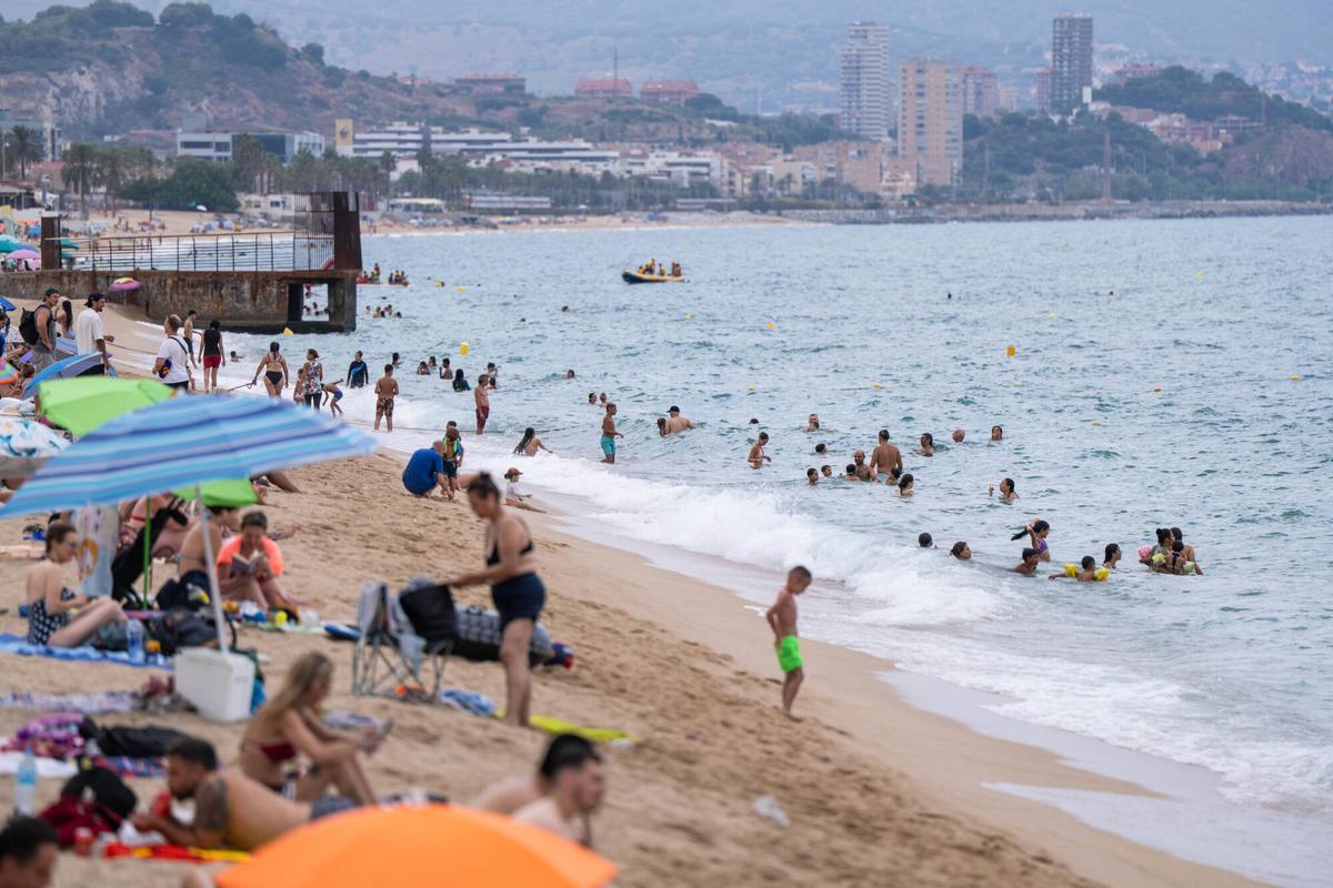 Personas refugiándose del calor en una playa de Badalona.
