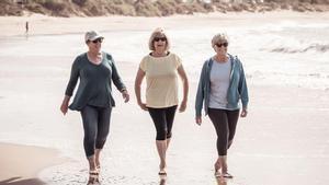 Tres mujeres caminan en la playa.