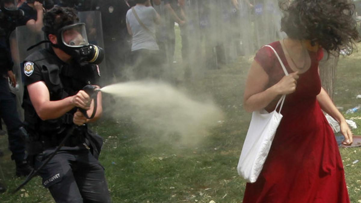 Un policía antidisturbios lanza gas lacrimógeno a una mujer vestida de rojo, en la plaza Taksim de Estambul.
