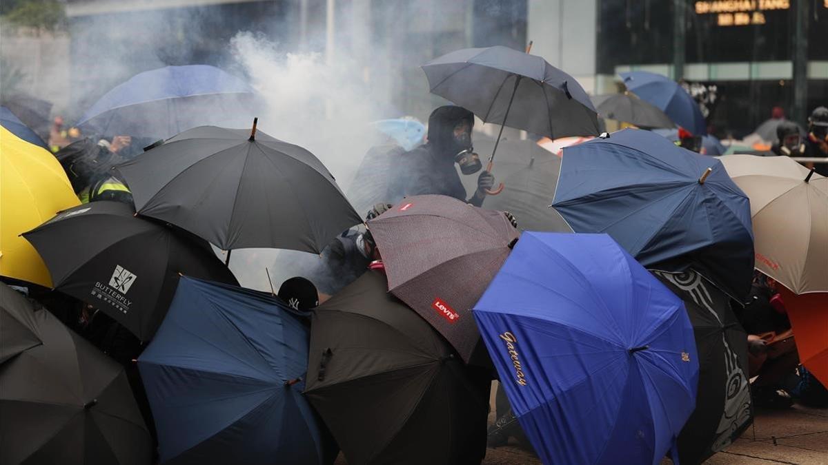 Varios manifestantes se protegen con paraguas de los gases lacrimógenos lanzados por la policía, este domingo en Hong Kong.