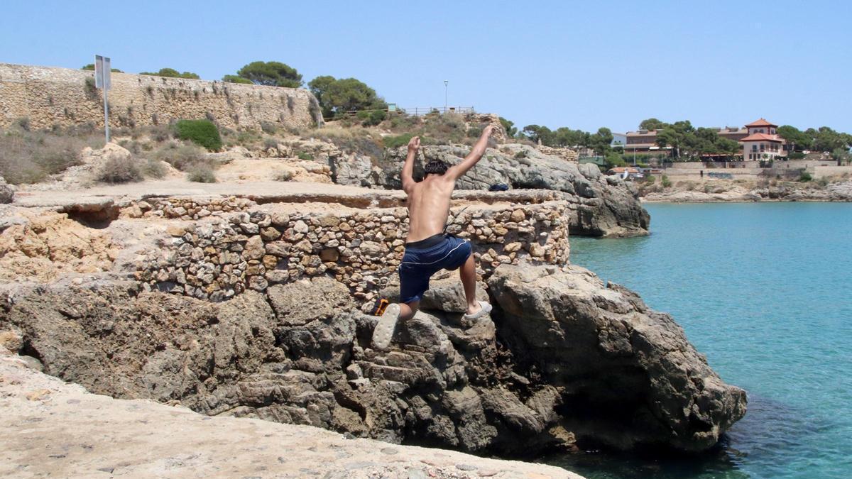Un menor salta des de les roques de la platja del Miracle de Tarragona, davant d'un cartell on està prohibit fer-ho.