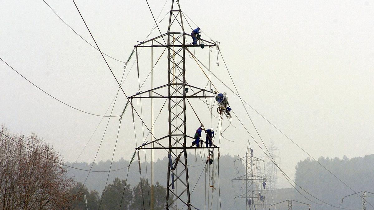 Operarios trabajan subidos en una torre eléctrica de alta tensión.