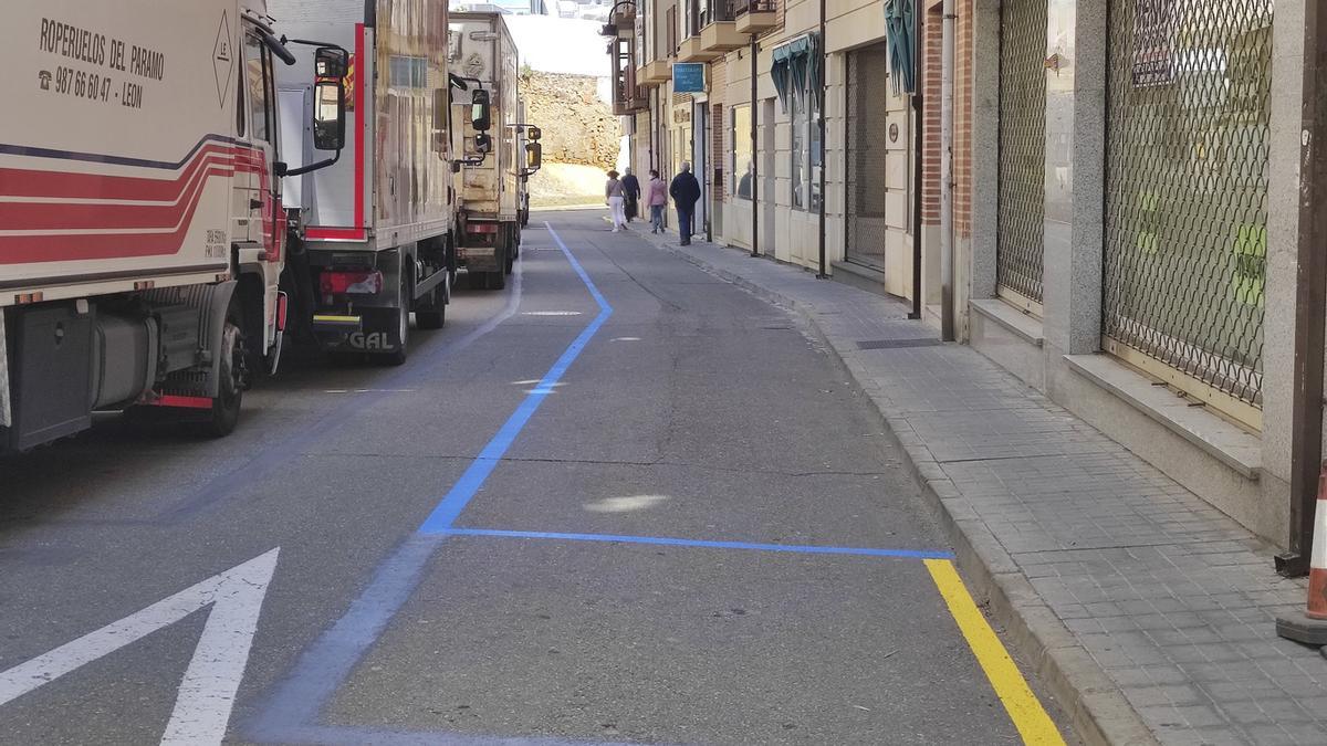 La franja de estacionamiento en zona azul ya pintada, aunque con meno dimensión, al lado de los edificios. A la izquierda camiones de verdura estacionados por ser día de mercado.
