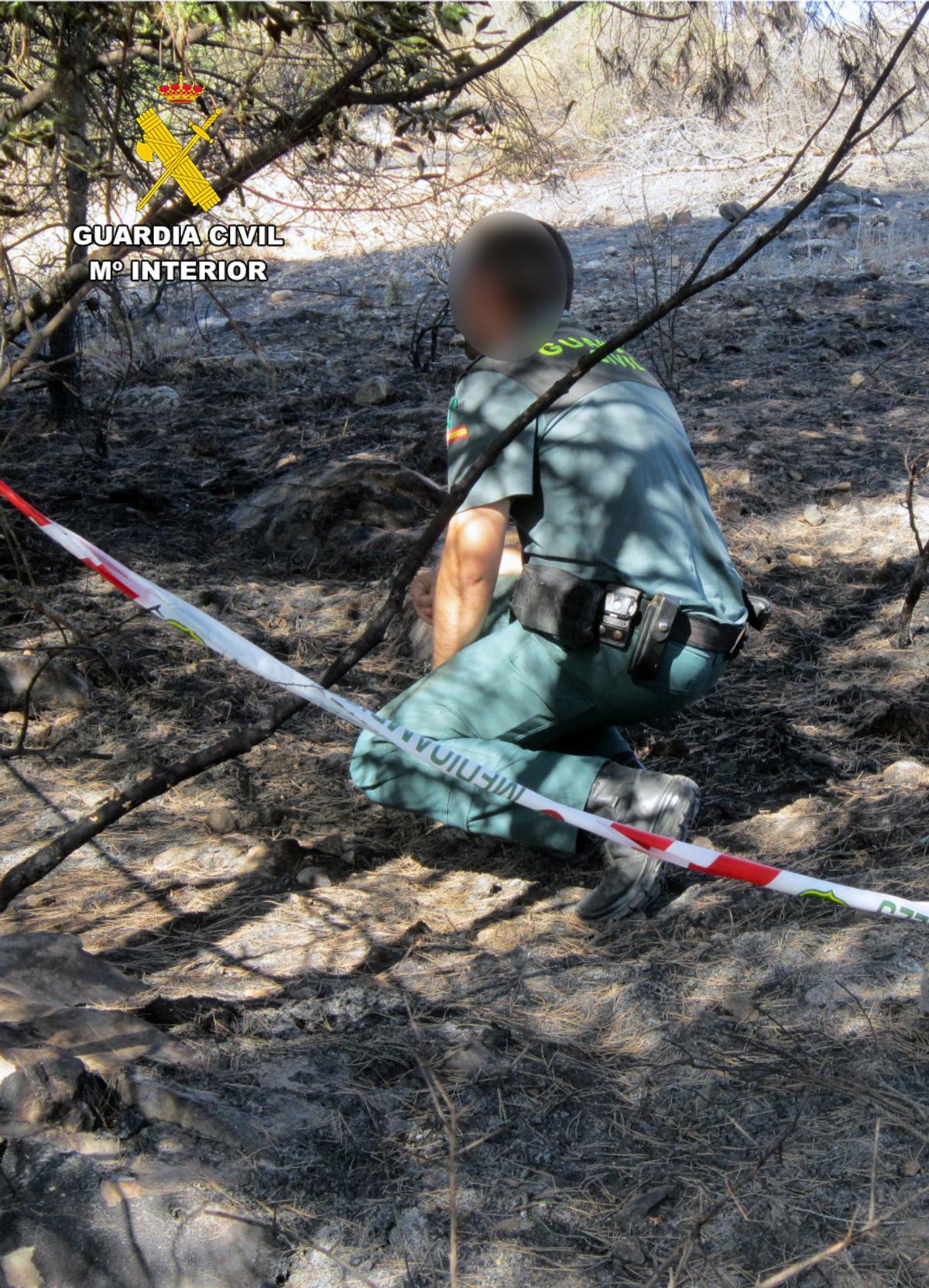 Un agente de la Guardia Civil revisa pruebas en la zona del incendio.