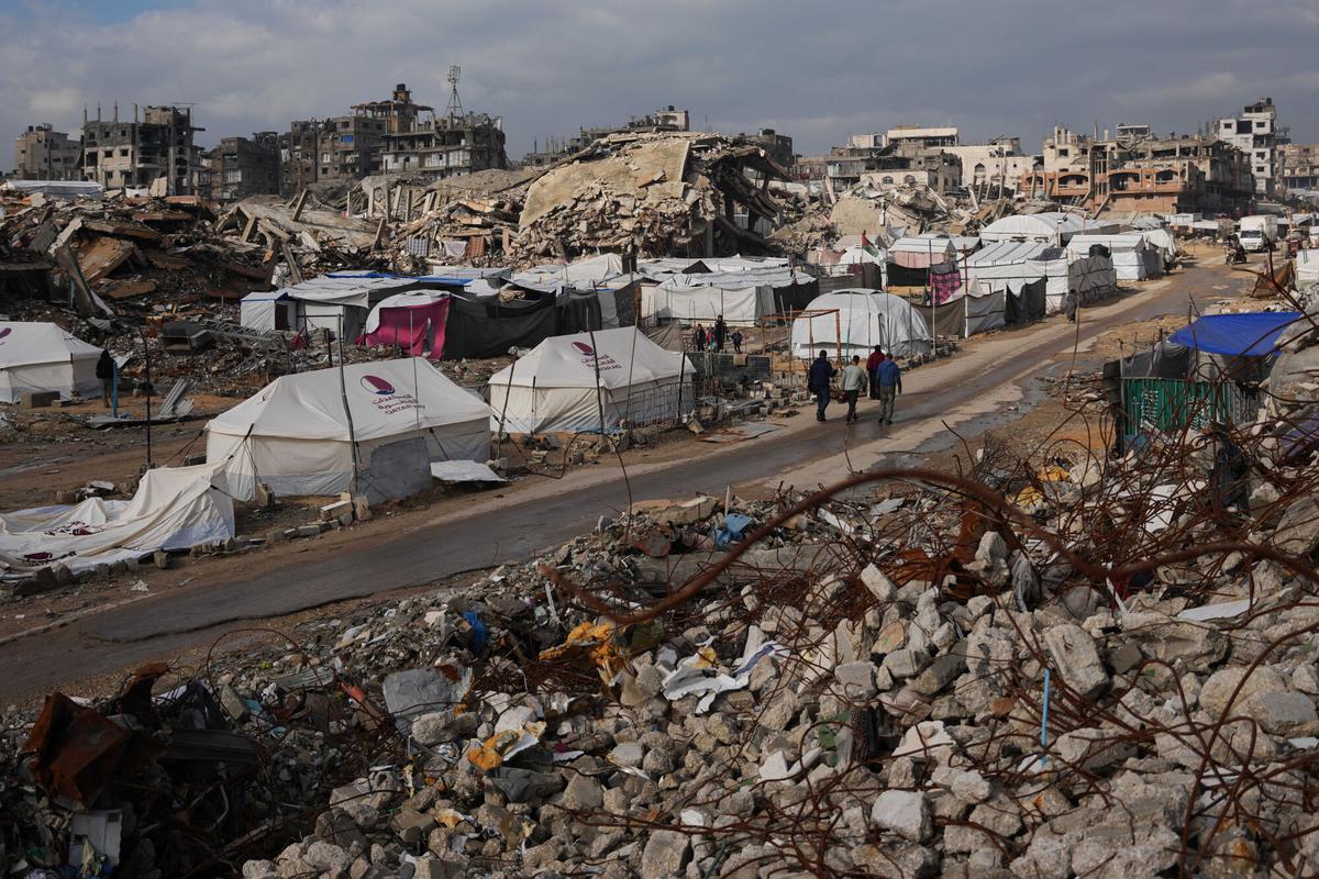 Palestinos caminan por una calle junto a un campamento de tiendas de campaña.