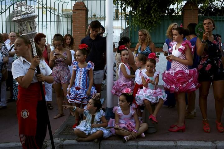 Girls, wearing traditional sevillana dresses, watch the procession of the El Carmen Virgin, on its way to be carried into the sea, in Malaga