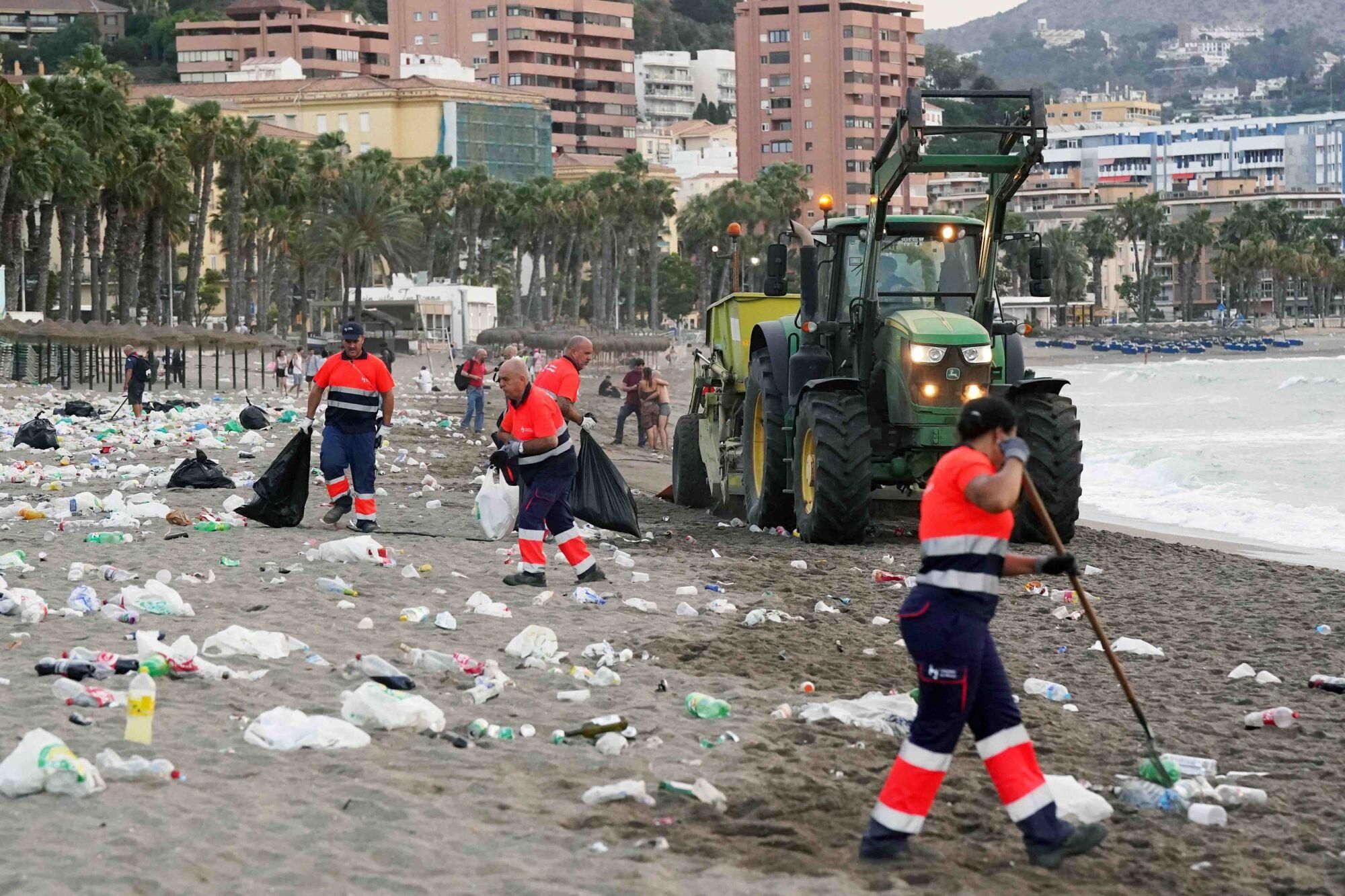 Varios operarios de la empresa de limpieza de Limasam, recogen los residuos de la playa de La Malagueta, tras la Noche de San Juan en Málaga 2025