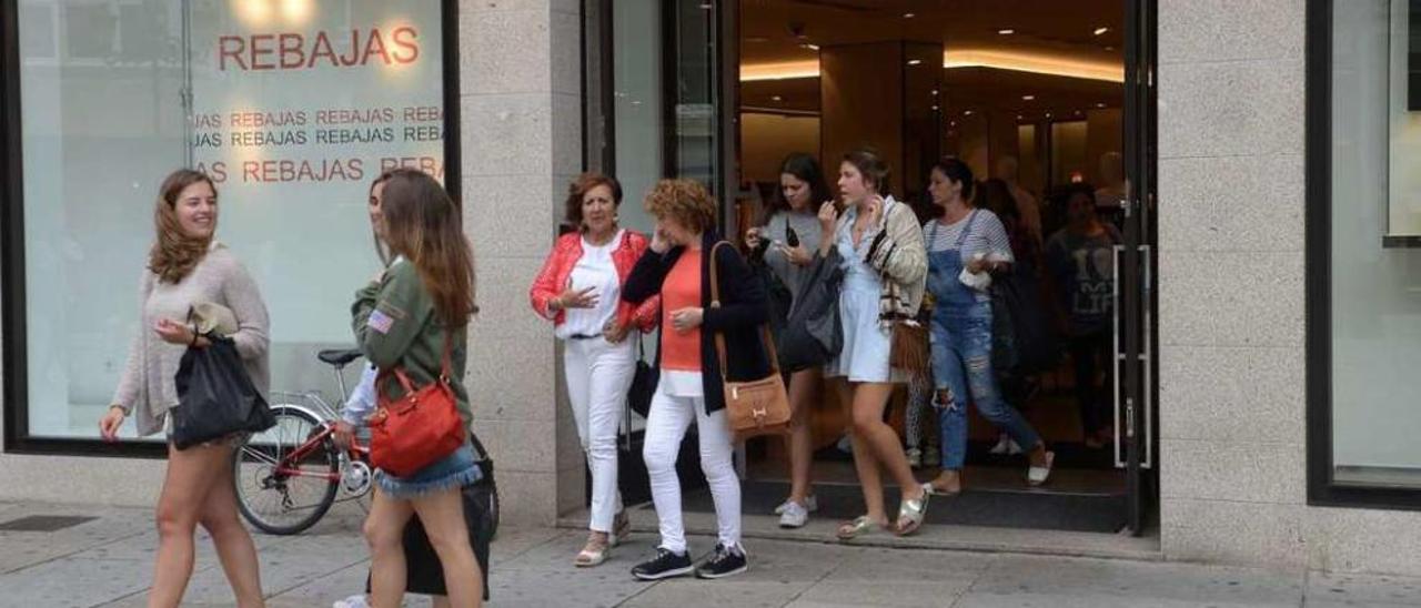 Varias clientas salen de una tienda de ropa que anuncia en su escaparate las rebajas.  // Noé Parga