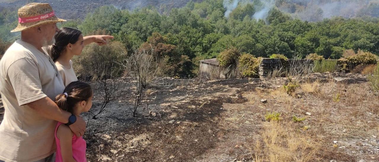 Camilo y dos menores miran el monte que aún humeaba ayer en Fondo de Vila, Boborás, uno de los lugares que estuvo en peligro.