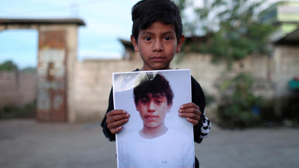 Un niño de Guatemala sostiene un cartel con la imagen de un familiar, encontrado en un camión junto con otros cadáveres de migrantes en Texas.