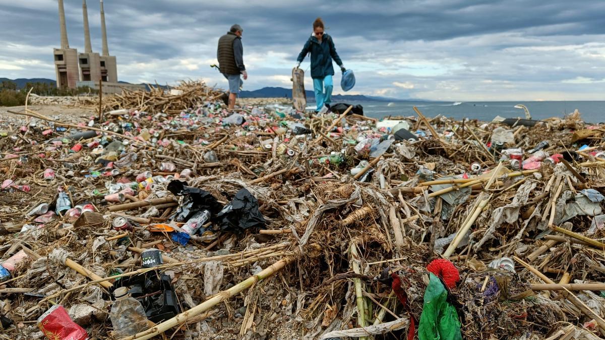 Dos voluntarios apartan basura acumulada en la desembocadura del río Besòs, este miércoles en Sant Adrià de Besòs.