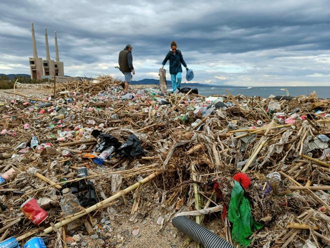 Dos voluntarios apartan basura acumulada en la desembocadura del río Besòs, este miércoles en Sant Adrià de Besòs.