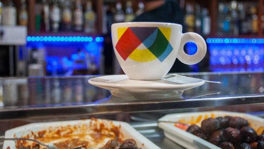 Una taza de café con un camarero al fondo en un bar.