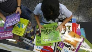 Dos niñas miran los libros de texto de su curso en la estantería de una librería.