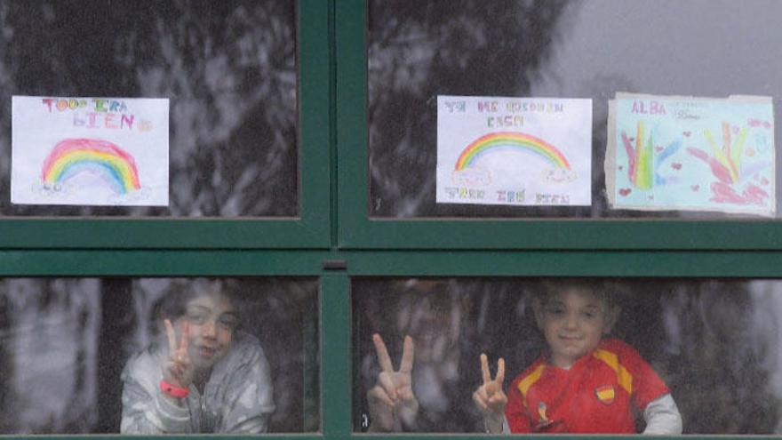 Dos niños en su domicilio de A Coruña durante la cuarentena, junto a dibujos de arcoiris.