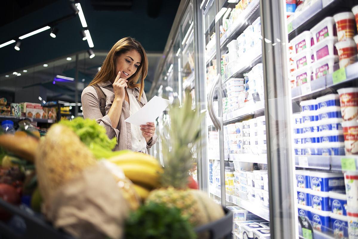 Una mujer repasando su lista de la compra en un supermercado.