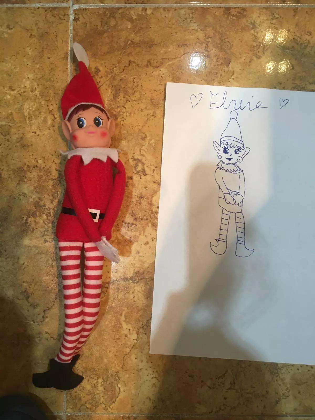 Un elfo de Navidad junto a un retrato suyo que ha dibujado por la noche.