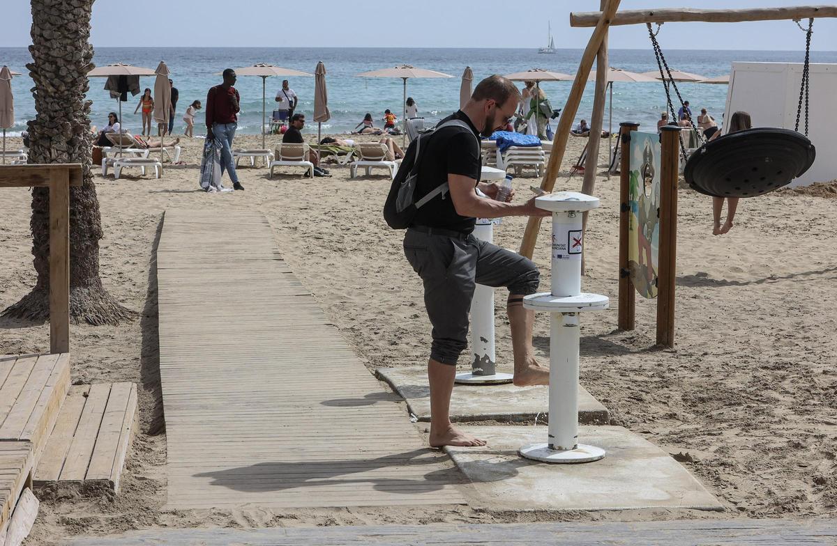 Un hombre utiliza el lavapiés en la playa del Postiguet de Alicante.