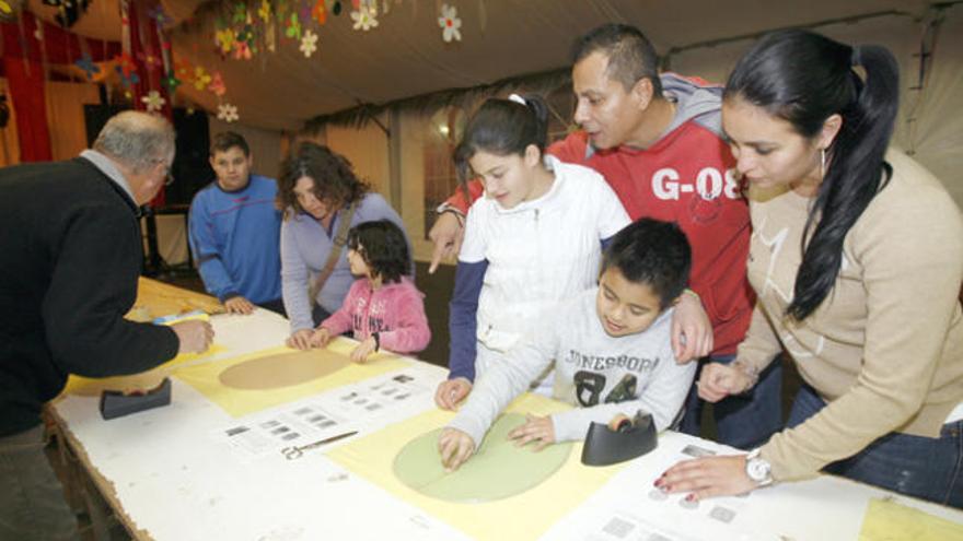 Madres acompañadas de sus hijos en la carpa municipal para elaborar sus propias cometas bajo el asesoramiento de los voluntarios del colegio Guillem de Montgrí y técnicos del Ayuntamiento.