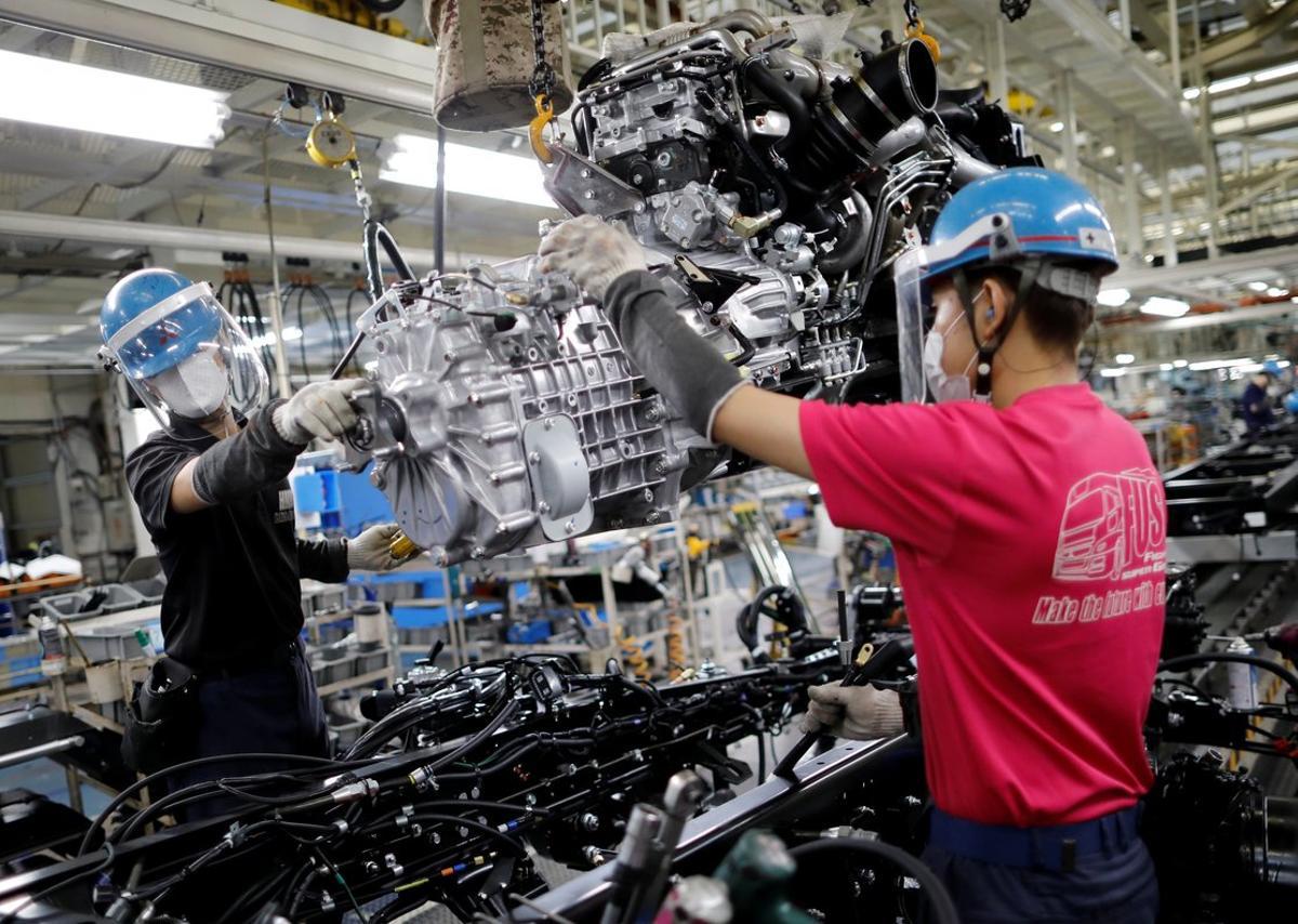 Employees wearing protective face masks and face guards work on the automobile assembly line as the maker ramps up car production with new security and health measures as a step to resume full operations, during the outbreak of the coronavirus disease (COVID-19), at Kawasaki factory of Mitsubishi Fuso Truck and Bus Corp., owned by Germany-based Daimler AG, in Kawasaki, south of Tokyo, Japan May 18, 2020.  REUTERS/Issei Kato