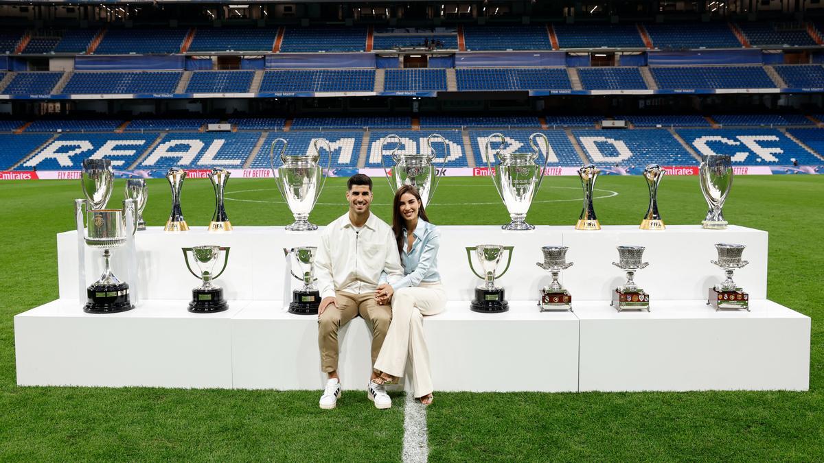 Marco Asensio posa con Sandra Garal con los diecisiete trofeos que ha conquistado en el Real Madrid.