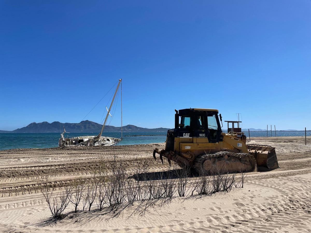Un tractor prepara la playa dels Tamarells con un velero varado en la orilla.
