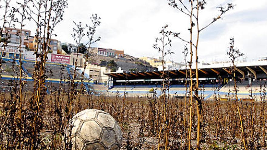 Un balón abandonado sobre el erial en que se ha convertido el césped resume la situación del Insular. A la derecha, arriba, un cuarto desvalijado y el local por donde se cuelan los okupas.  ANDRÉS CRUZ