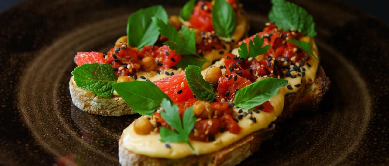 Tostada de hummus con pimientos asados aliñados, pomelo, garbanzos crujientes, sésamo y hierbas frescas del resturante Brevet.