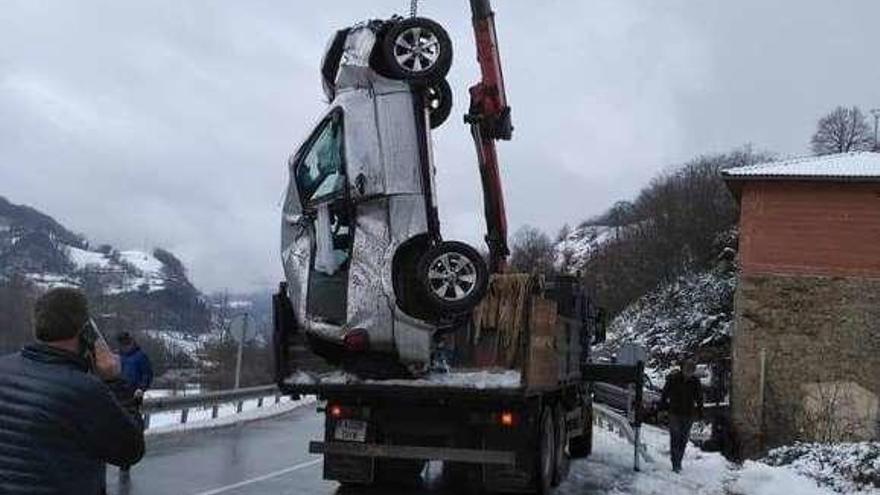 Una grúa iza el coche siniestrado en Aller. A la derecha, la carretera de San Isidro, ayer.